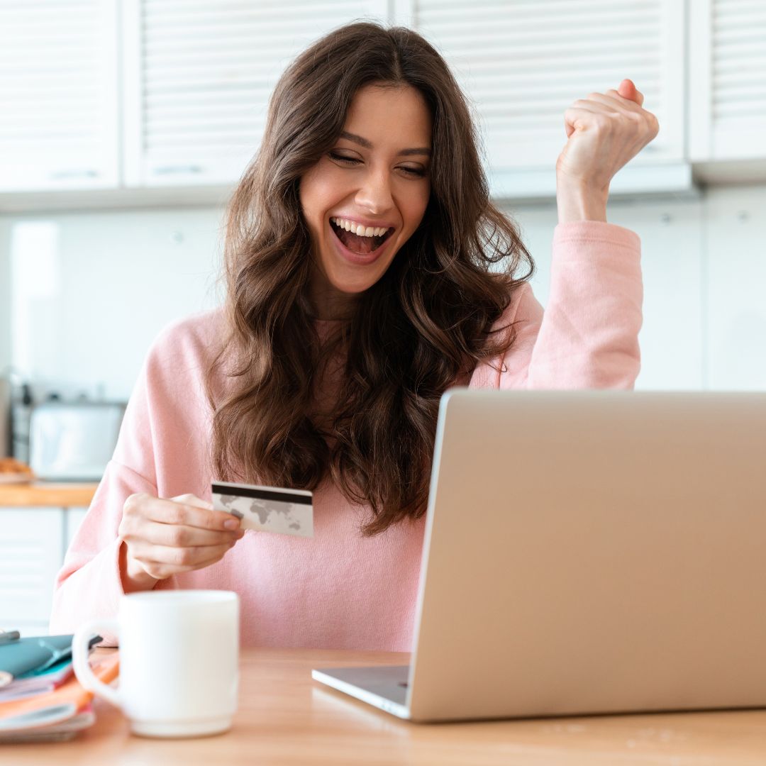 You woman cheering with credit card in hand while looking at a laptop